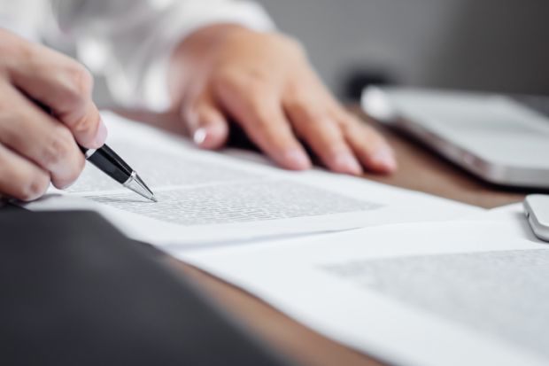 A hand clasps a pen, writing on a document