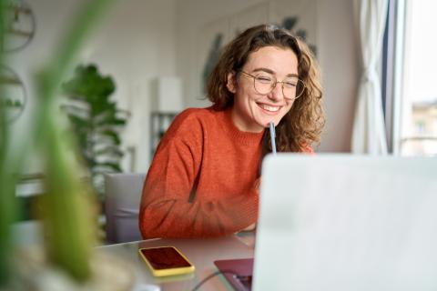 A young woman looking happy as she works at a laptop